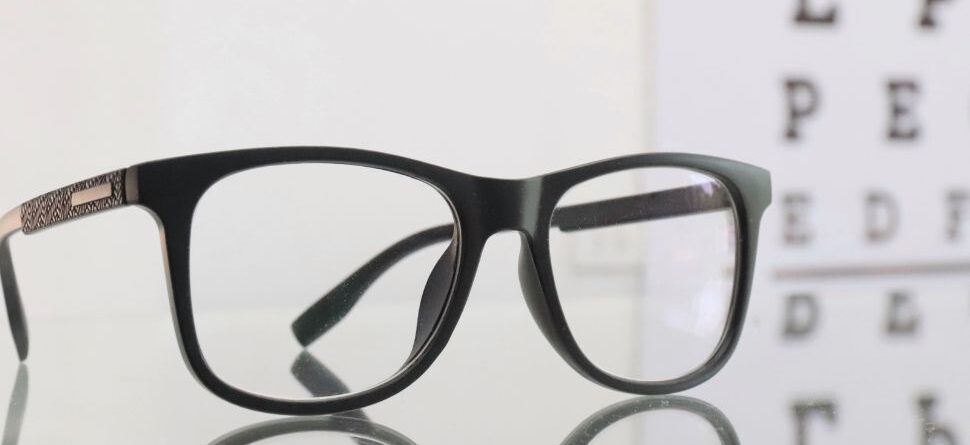 Gafas negras de diseño clásico frente a un cartel de optometría, simbolizando la importancia de un buen cuidado visual y revisiones periódicas.