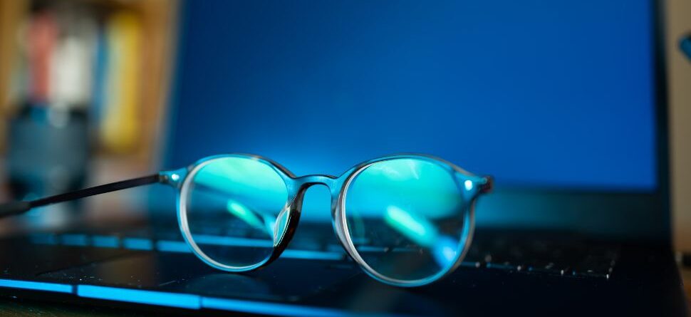 Gafas descansando sobre el teclado de un portátil con la pantalla encendida en azul, resaltando la importancia del filtro de luz azul para proteger la vista.