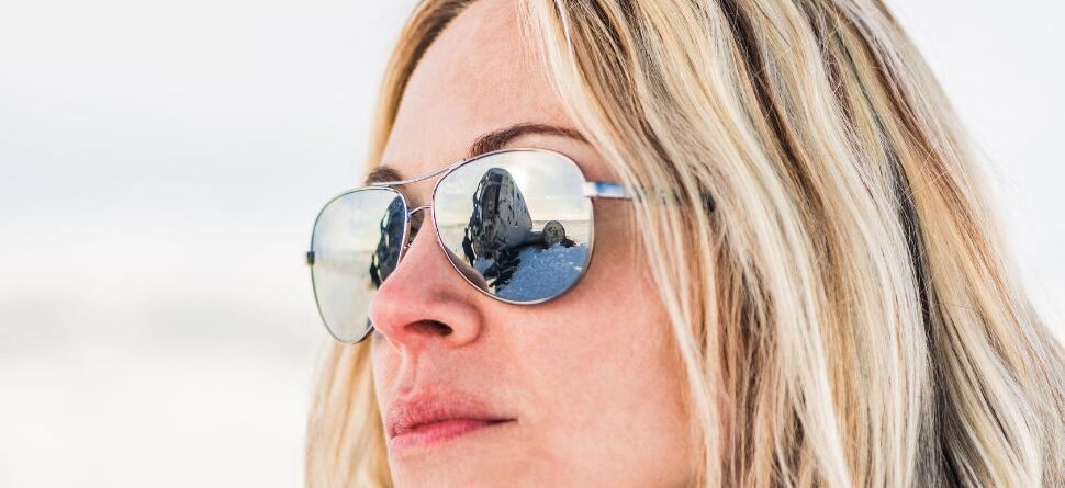 Mujer usando gafas de sol polarizadas, reflejando un paisaje nevado, ideal para actividades al aire libre con alta exposición solar.