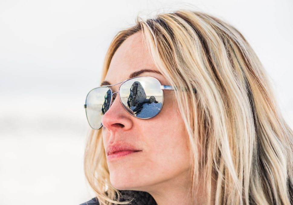 Mujer usando gafas de sol polarizadas, reflejando un paisaje nevado, ideal para actividades al aire libre con alta exposición solar.