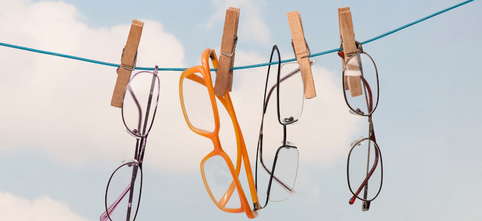 Varios pares de gafas de sol colgadas en una cuerda con pinzas al aire libre, mostrando diferentes estilos de armazones bajo un cielo despejado.