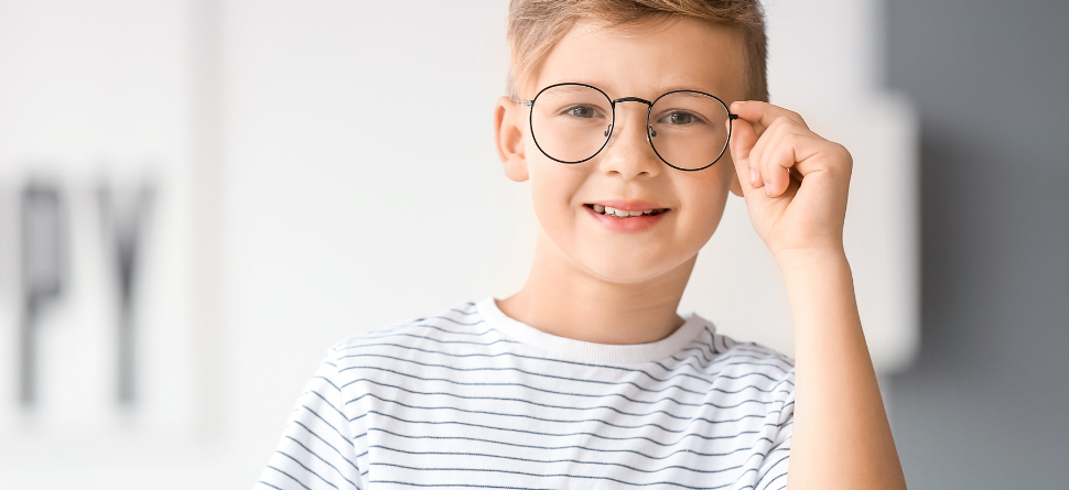 Niño sonriente con gafas en un entorno luminoso, mostrando la importancia de llevar gafas graduadas para una visión clara desde la infancia.