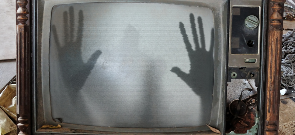 Imagen de un televisor antiguo con sombras de manos en la pantalla, creando un efecto aterrador. Ideal para maratones de películas de terror y ambientar la spooky season.
