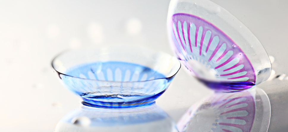Dos lentillas decorativas de Halloween, una con diseño azul y la otra con un patrón púrpura, sobre una superficie reflectante. Ideales para disfraces impactantes.