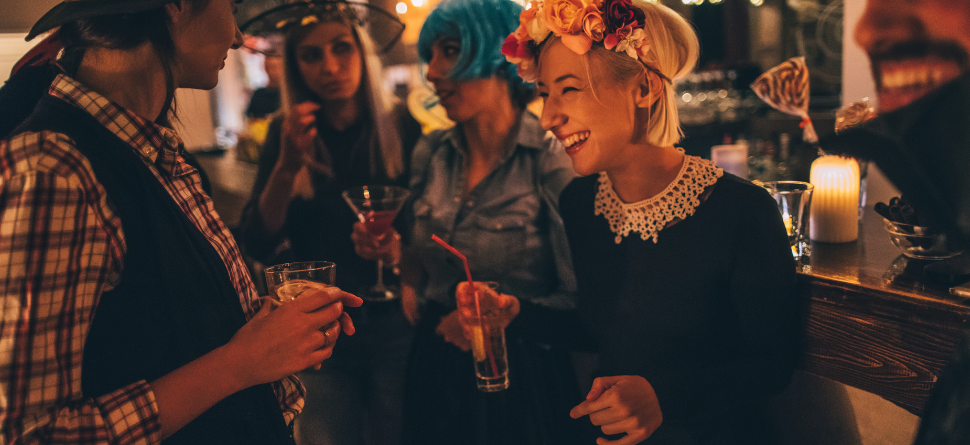 Grupo de amigos en una fiesta de Halloween, todos disfrazados y disfrutando en un ambiente cálido con bebidas. El uso de gafas protege sus ojos en eventos nocturnos, donde la iluminación es baja y puede afectar la vista.