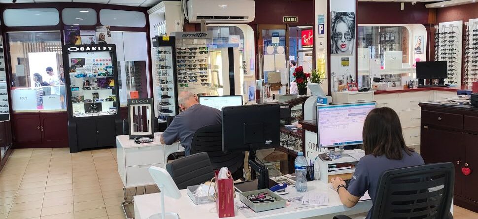 Vista general de Óptica Cosmos, mostrando una amplia gama de gafas de marcas reconocidas como Gucci, Oakley y Ray-Ban, con personal trabajando en un entorno moderno.