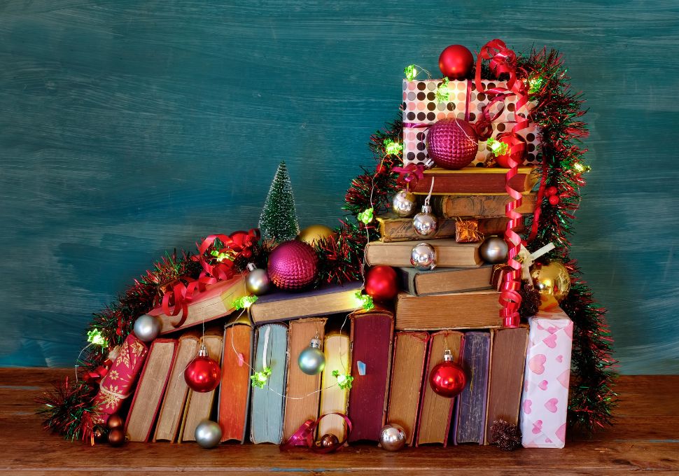 Imagen de libros decorados con adornos navideños: Una pila de libros decorada con luces, bolas y guirnaldas navideñas, creando un ambiente festivo y literario. Perfecto para transmitir el espíritu navideño relacionado con la lectura y los regalos ideales para lectores.