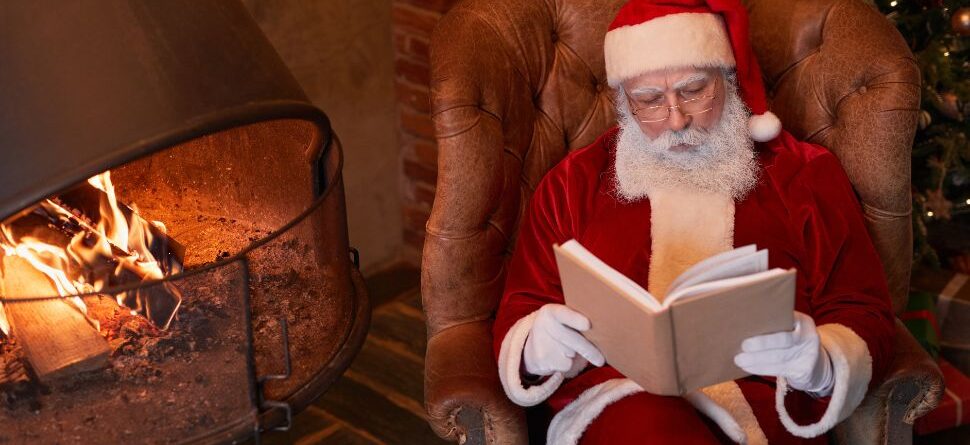 Imagen de Papá Noel leyendo un libro junto a una chimenea: Papá Noel sentado en una silla de cuero, disfrutando de la lectura junto a una cálida chimenea decorada para Navidad. Un momento acogedor que destaca la importancia de regalar comodidad y cultura en estas fechas.