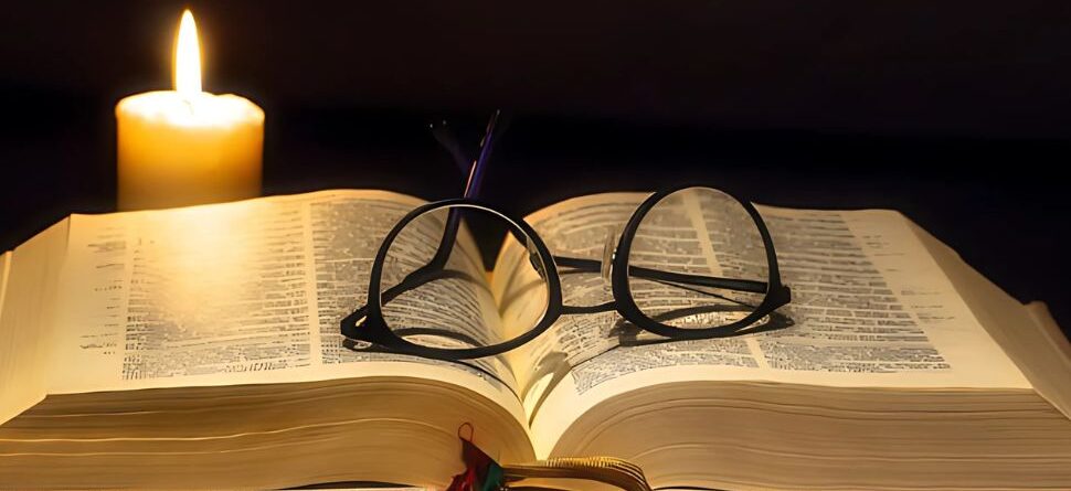 Gafas redondas colocadas sobre un libro abierto iluminado por una vela, evocando tranquilidad y momentos de lectura nocturna.