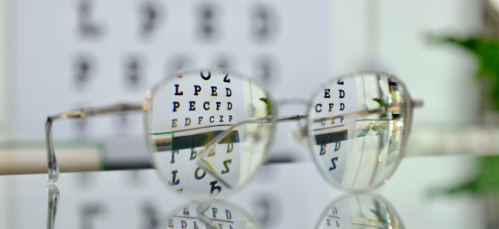 Primer plano de unas gafas frente a un cartel de optometría con letras, mostrando la claridad que ofrecen las lentes progresivas en diferentes distancias. Ideal para destacar los beneficios de las lentes progresivas en la visión diaria.