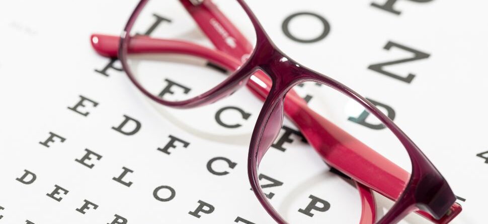 Gafas de montura roja sobre una tabla optométrica en Óptica Cosmos Tenerife. Resalta la precisión en la graduación de lentes para mejorar la visión en el día a día.