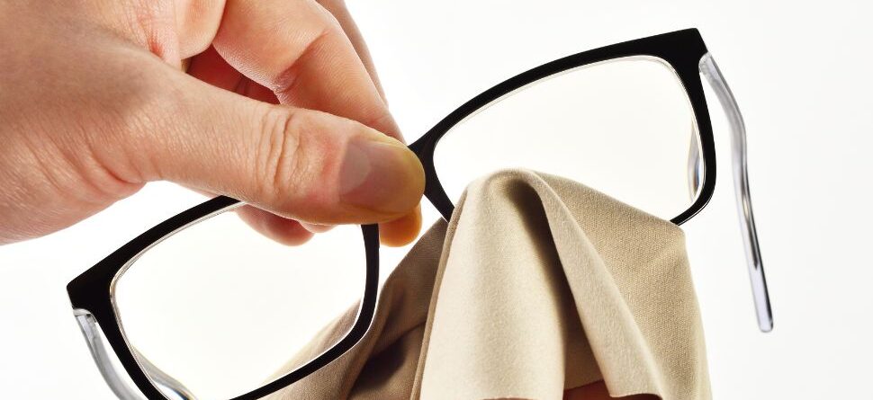 Detalle de manos sosteniendo unas gafas y limpiando las lentes con un paño suave, técnica adecuada recomendada por Óptica Cosmos La Laguna.