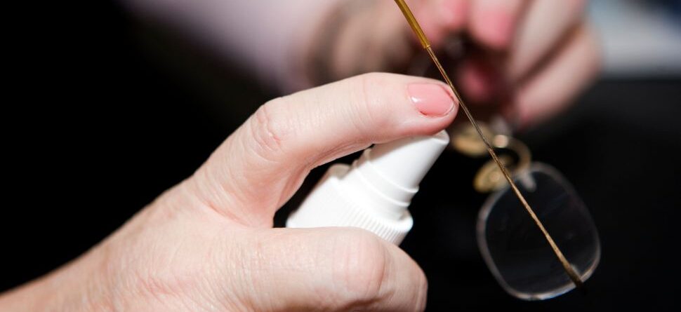 Primer plano de unas manos usando un spray especializado para limpiar gafas ópticas, promoviendo su cuidado correcto. Óptica Cosmos La Laguna.